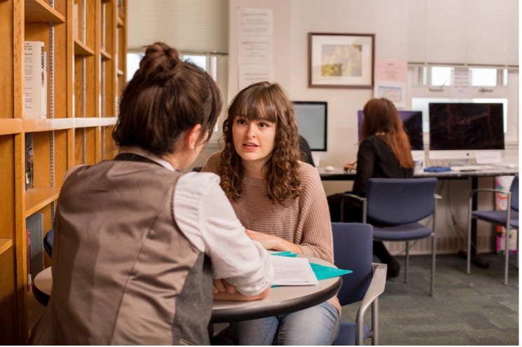 Two girls talking with a book between them.