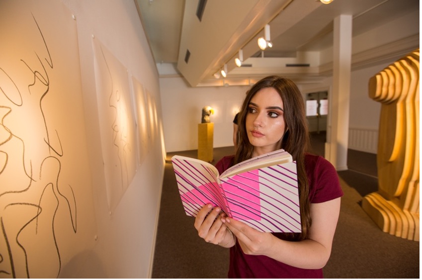 Student reads a book while looking at an art display.