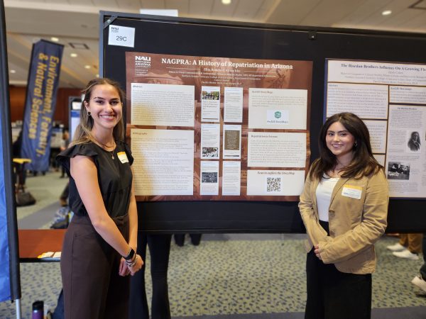 Two dark haired women, one taller than the other, stand with their brown and rust colored poster. 