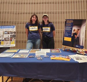 Two students stand in front of a marketing board for CCS.