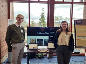 Two students stand in front of a digital monitor.
