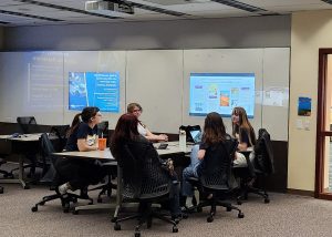Students and guests sit in front of a digital monitor