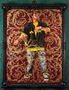 The image shows a Black man in a green and yellow shirt against a gold and burgundy background.