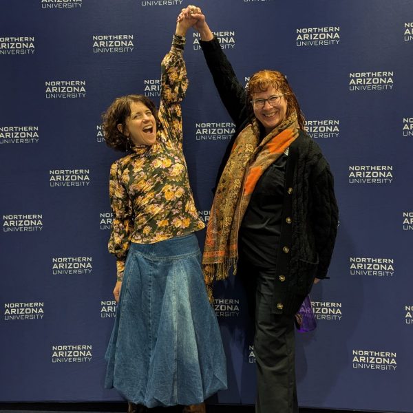two smiling women hold their hands high in celebration