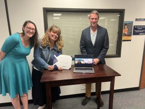 Several professors pose with a laptop and a certificate.