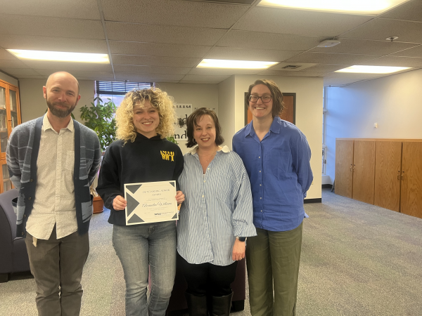 three faculty smile around a student with a certificate