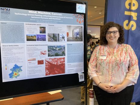 student in glasses smiles in front of a poster