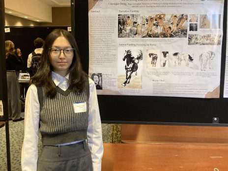 student in a vest presents their poster