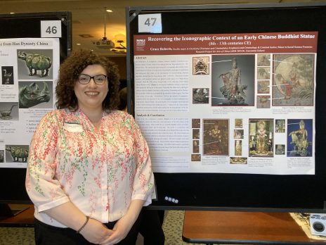 student in glasses smiles in front of their poster
