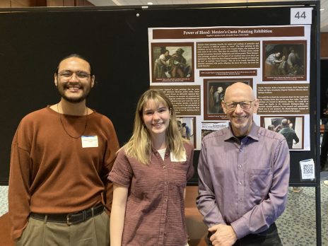 three people smile in front of a poster