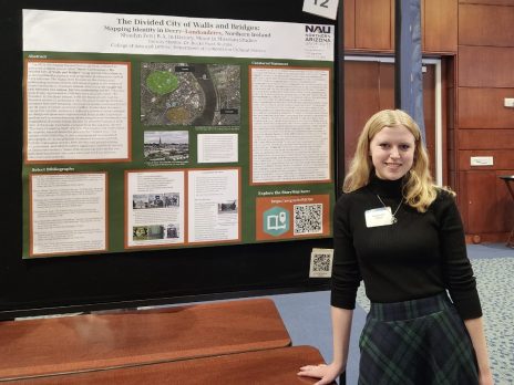 a student leans on one hand, smiling in front of a poster