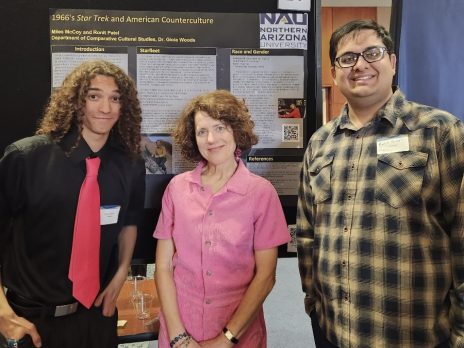 three people smile in front of a poster
