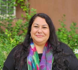 This image depicts a woman with long dark hair wearing a black shirt and multicolored scarf.