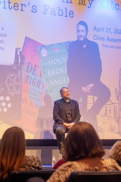 Luis Urrea sits on a stool on stage.