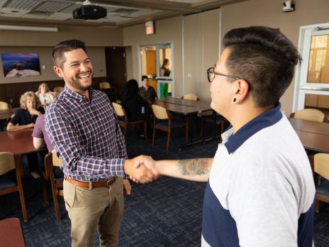 Two N A U alumni shaking hands and smiling.
