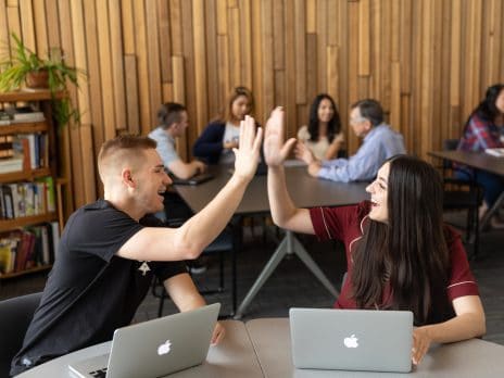 male and female students giving each other a high five while sharing a table 