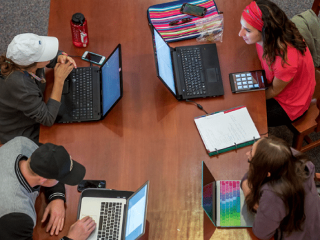 Four students sitting together at a table with their laptops.