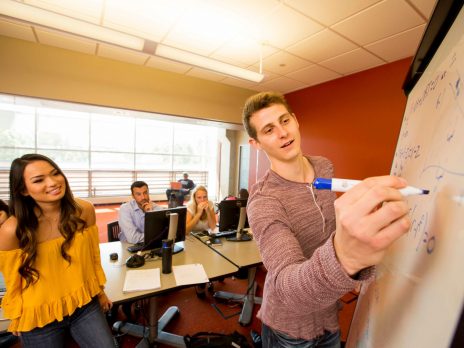 NAU student writing on a whiteboard as another student looks on