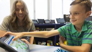 A child is navigating an augmentative and alternative speech device as a service provider looks on to give guidance when necessary.