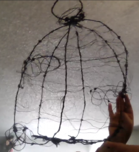 photo of an artistic version of a birdcage made from twine pictured with a hand holding it.