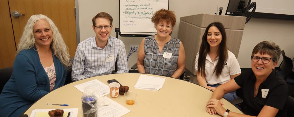 5 adults sitting around a round table smiling.