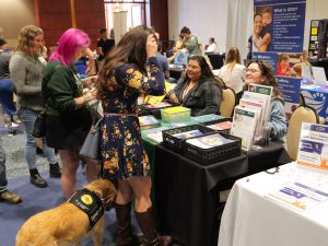 group of people in a busy exhibit hall person in foreground has a support dog