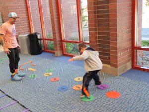 A man works smiles as a young boy runs through an accessible obstacle course