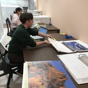A young man and a young woman sitting at a table handling posters of landscape photography.
