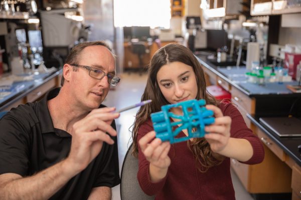 Tim Becker and a student is holding up a 3D printed model.