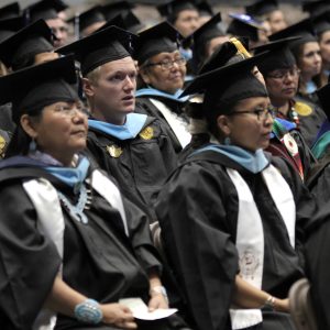 various graduates in their caps and gowns sit facing forward