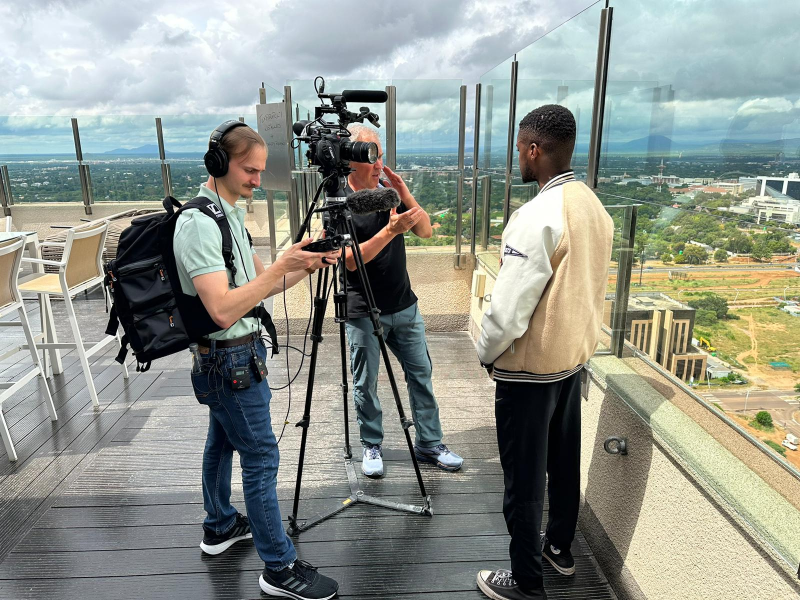 A behind-the-scenes shot of Professor Bill Carter and Angel Rodriguez shooting an interview with Prince Chidzala
