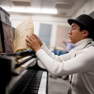 student reads through music book while sitting in front of piano