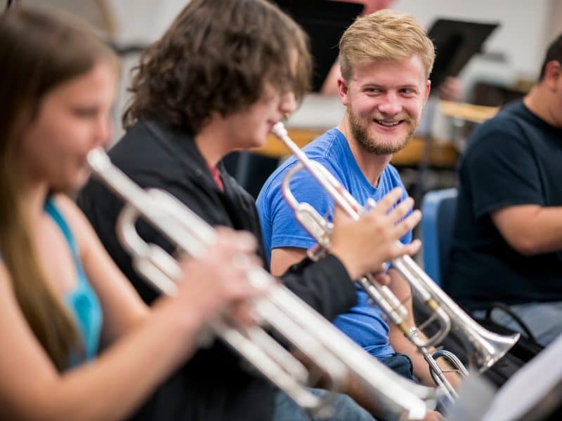 two students play trumpets while another students watches