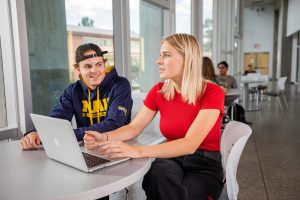 Two students sitting in the student union collaborating over something on a computer.