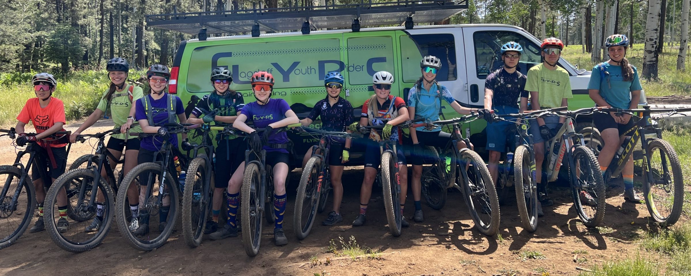 A group of FLYERS mountain bikers rest on a green van.