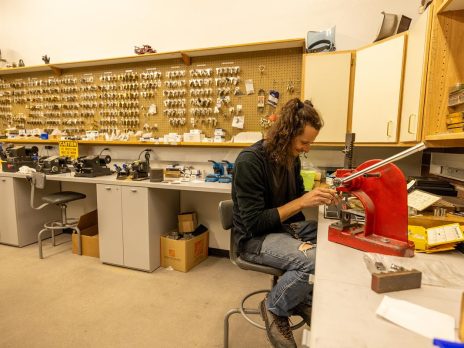 A person working on a key-cutting machine in the university lockshop with many key blanks stored in the background.