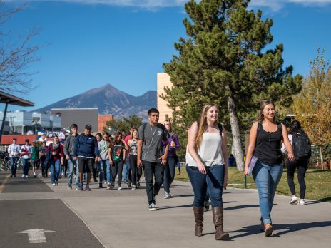 2 girls walking on main campus path with other people behind them and the San Fransisco peaks on a clear sky day.