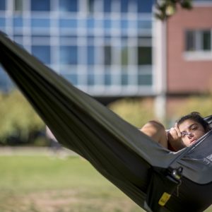 Woman laying in hammock on campus studying