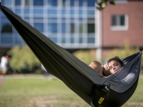 Woman laying in hammock on campus studying