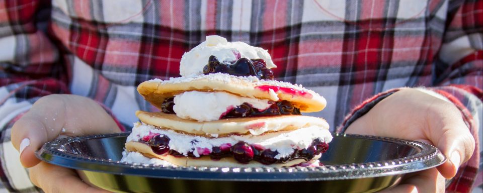student in flannel shirt holding pancakes layered with whipped cream and berries