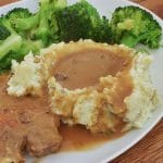 Mashed potatoes and gravy on a plate with meat and broccoli