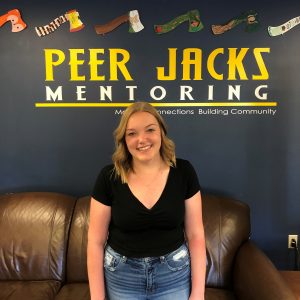 A student stands in front of text reading "Peer Jacks Mentoring"