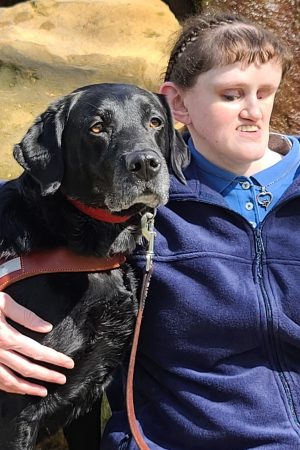 Picture of Nicole and her black Labrador guide dog Rivet sitting together at a fountain