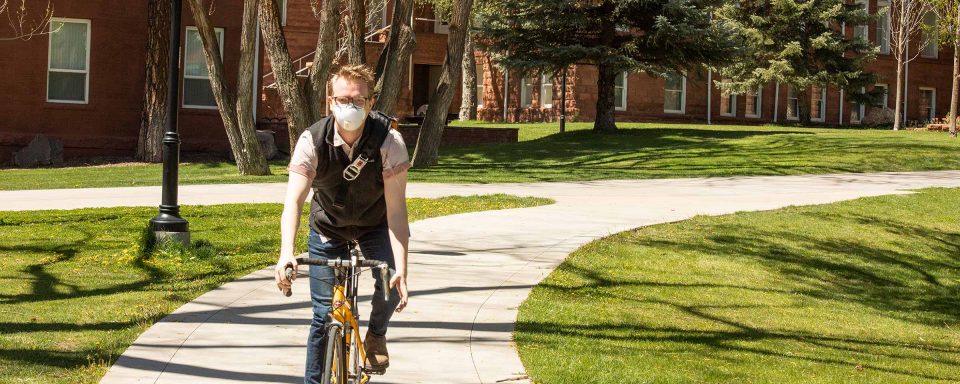 NAU student riding a bike on campus wearing a mask.