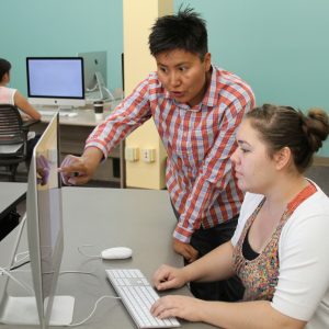 cline library employee pointing at computer screen to help student in the media lab