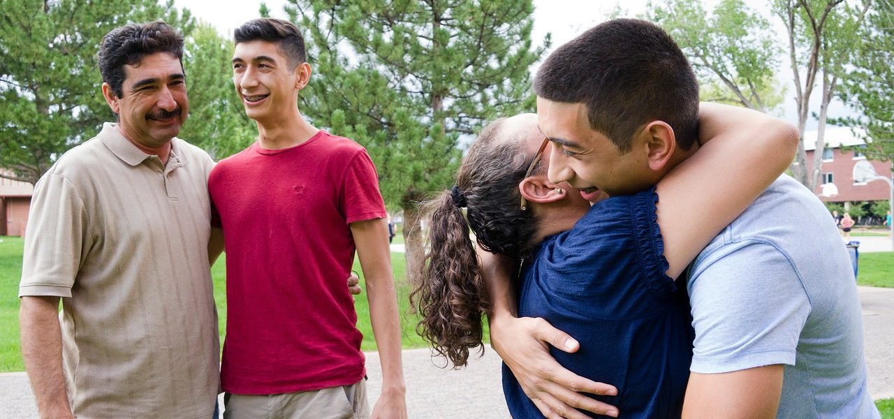 A mother hugs her child while the father and a sibling stand nearby, smiling.