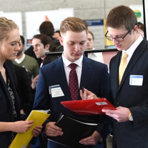 three students dressed in suits comparing resumes at career fair