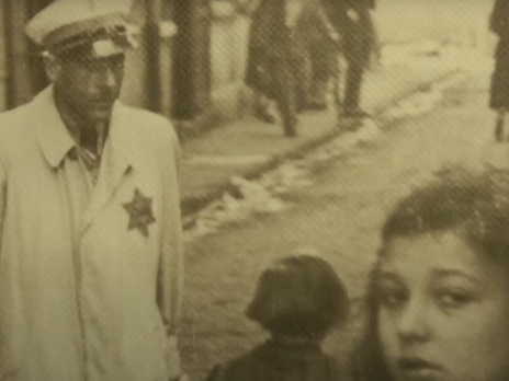 screen shot from interview showing a panel in the exhibit, sepia man with star on his coat and girls face passing him in the street