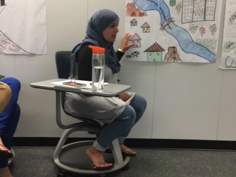 student in head scarf with project on the wall