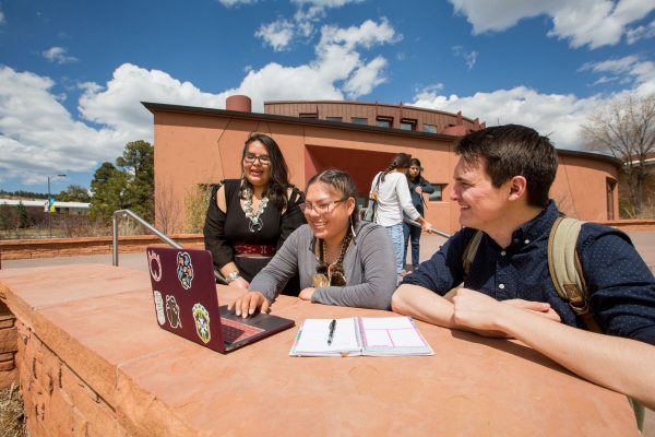three students outside the NACC, on a laptop, looking at the screen together